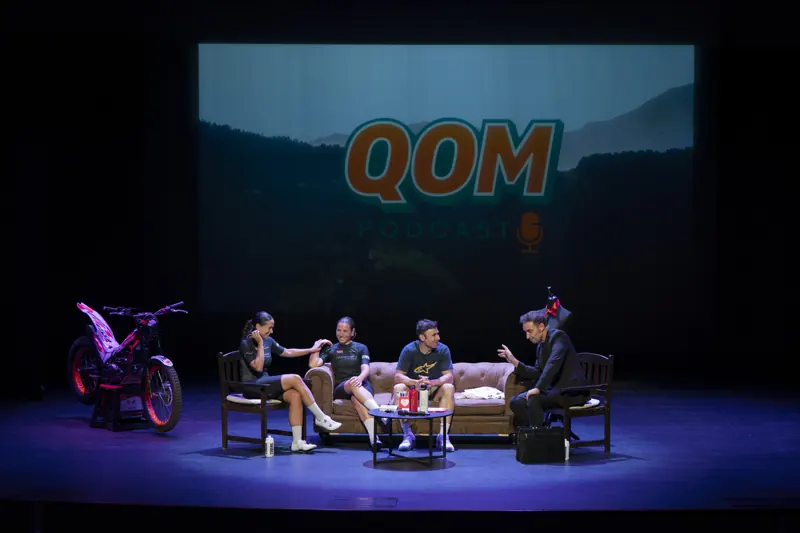QOM Podcast en directo sobre un escenario, con la pantalla gigante del logotipo